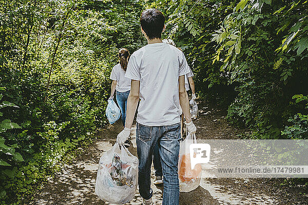Rückansicht von männlichen und weiblichen Umweltschützern  die mit Plastiktüten durch einen Park gehen