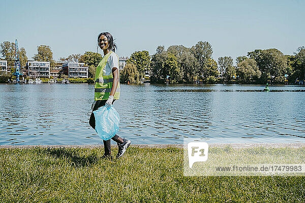 Porträt einer jungen Frau  die mit einer Plastiktüte in der Hand am See spazieren geht