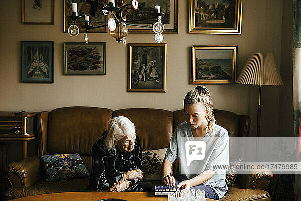 Eine ältere Frau und eine Mitarbeiterin des Gesundheitswesens betrachten eine Hausapotheke im Wohnzimmer
