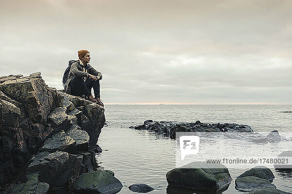 Nachdenklicher Mann  der auf einem Felsen am Meer sitzt