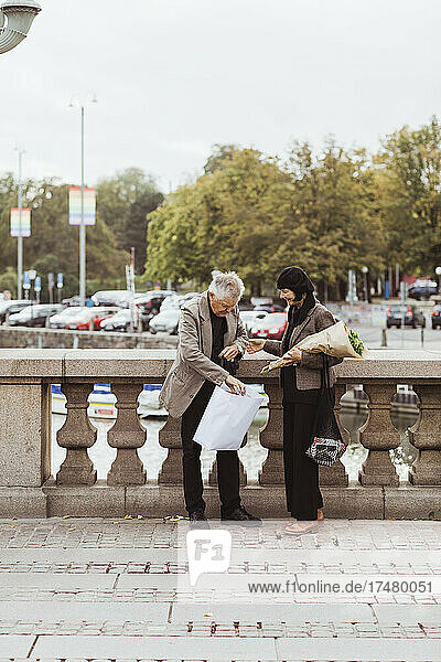 Älteres Paar  das auf einer Brücke in der Stadt steht und in eine Einkaufstasche schaut