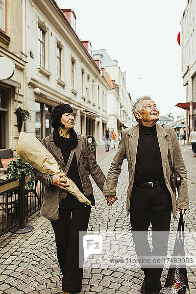 Älteres Paar hält sich an den Händen  während es im Urlaub die Stadt erkundet