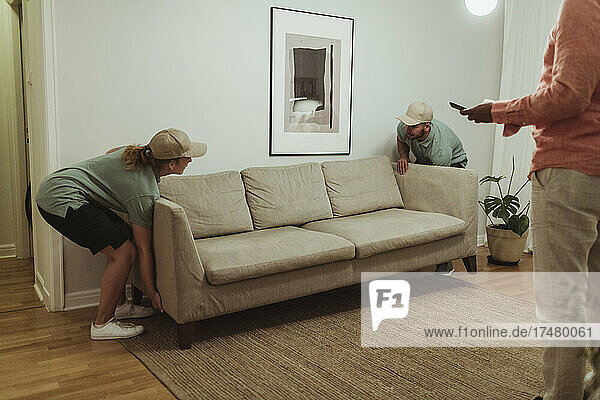 Männliche und weibliche Mitarbeiter tragen ein Sofa in das Wohnzimmer eines Kunden