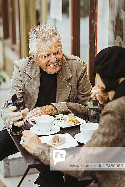 Lächelnder älterer Mann teilt Smartphone mit Frau in Café