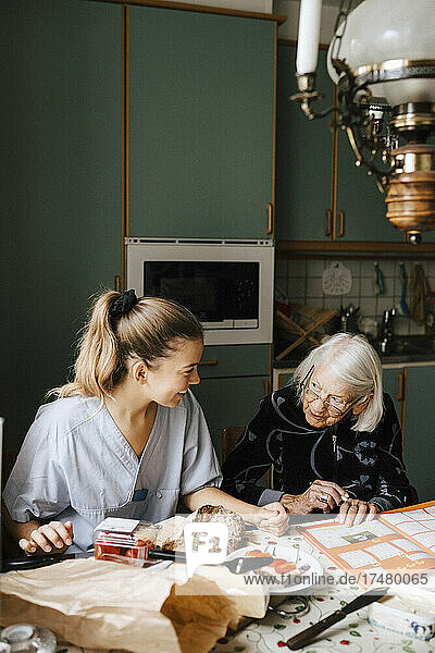 Lächelnde Krankenschwester unterrichtet ältere Frau am Esstisch in der Küche