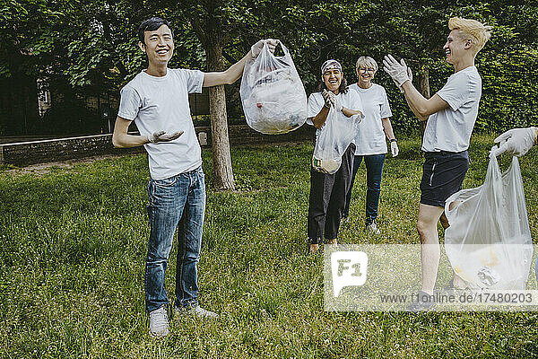 Glückliche männliche und weibliche Freiwillige klatschen für eine junge Aktivistin  die eine Plastiktüte im Park hält