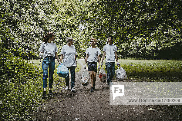 Weibliche und männliche Freiwillige unterhalten sich beim Spaziergang mit Plastiktüten im Park