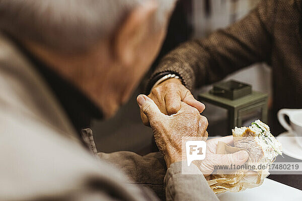 Älterer Mann hält die Hand einer Frau  während er am Wochenende in einem Café ein Sandwich isst