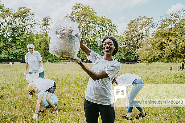 Porträt einer Umweltschützerin  die Plastikmüll zeigt  während Freiwillige im Park putzen