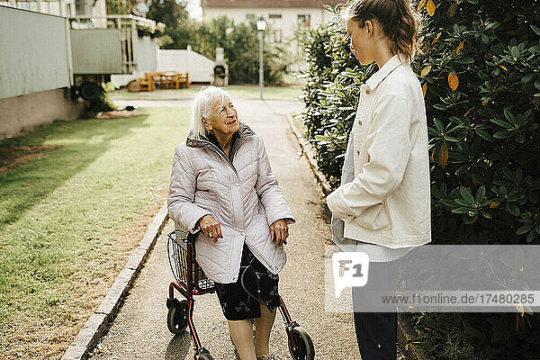Female nurse talking with senior woman leaning on walker at front yard