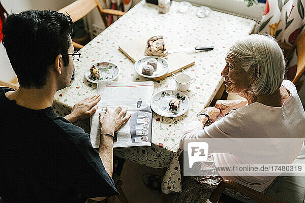 Blick von oben auf Krankenpfleger und ältere Frau  die am Esstisch Zeitung lesen