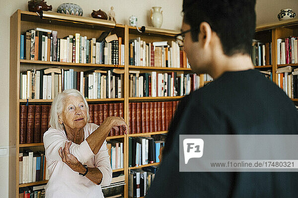 Ältere Frau beim Sport  während ein Pfleger ihr im Wohnzimmer hilft