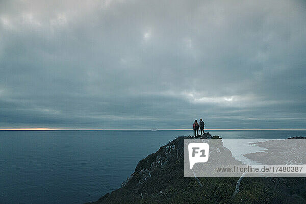 Male friends standing on rock formation during adventurous trip at dusk