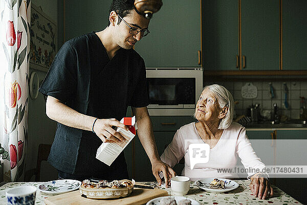 Männlicher Pfleger mit Safttüte  der neben einer älteren Frau in der Küche steht