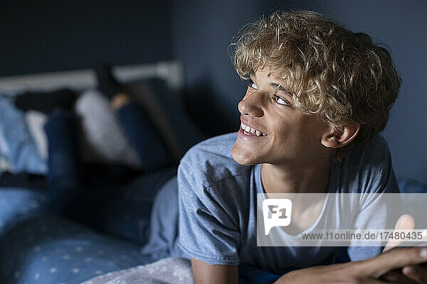 Blonder Junge lächelnd auf dem Bett liegend im Schlafzimmer zu Hause