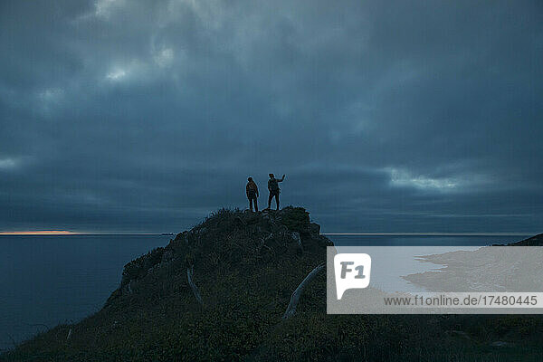 Männer auf dem Gipfel eines Hügels gegen den bewölkten Himmel in der Abenddämmerung
