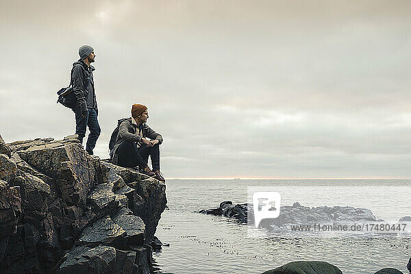 Male friends on rocks at beach during sunset
