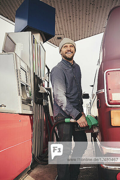 Lächelnder Mann beim Tanken eines Campingbusses an einer Tankstelle