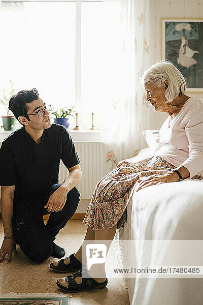 Ältere Frau im Gespräch mit einem jungen Mann aus dem Gesundheitswesen im Schlafzimmer zu Hause