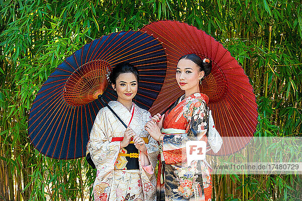 Portrait of two women wearing kimonos and holding parasols in park