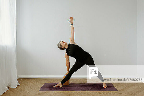 Woman performing Trikonasana on yoga mat at home