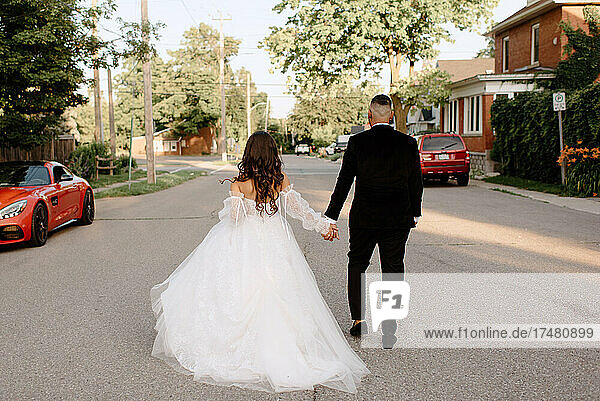 Rear view of bride and groom walking on suburban street