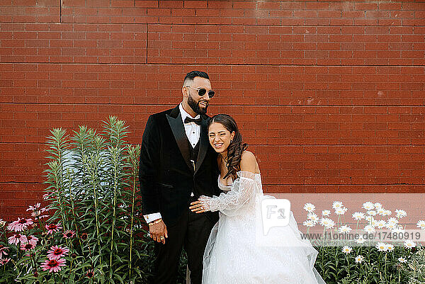Smiling bride and groom against brick wall and flowers