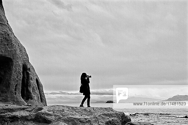 Frau fotografiert am Meer  Frau macht Foto  Fotografierende  fotografieren  Fotohobby  Amateurfotograf  Frau macht Landschaftsfoto  Frau fotografiert auf Felsen am Strand  Almeria  Andalusien  Spanien  Europa