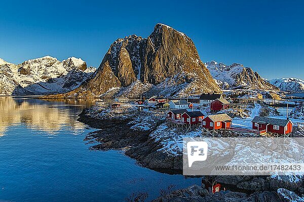 Winterliche skandinavische Landschaft mit erleuchteten roten Häusern  Meer  Berge  Schnee  Hamnøy  Nordland  Lofoten  Norwegen  Europa
