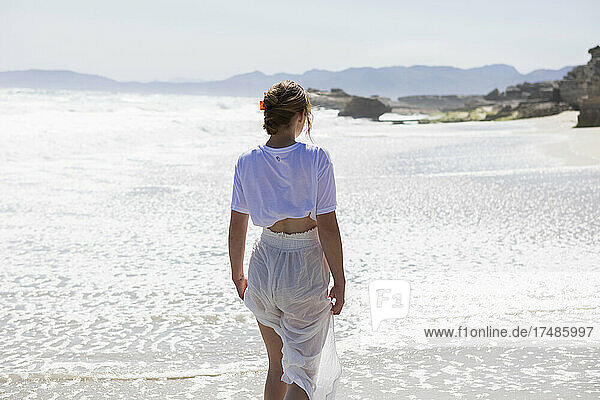 Teenager-Mädchen allein an einem Sandstrand in Südafrika am Rande des Wassers mit Blick auf die Küste