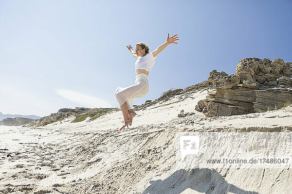 A teenage girl leaping from a sand dune into the soft sand below.