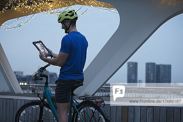 Mann auf dem Fahrrad  Videochat mit digitalem Tablet in der Stadt bei Nacht