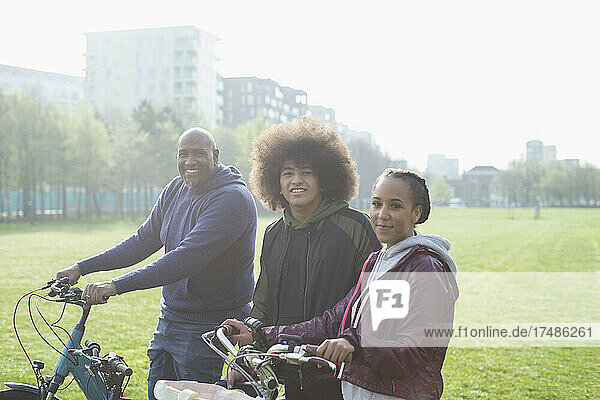 Porträt glückliche Familie mit Fahrrädern in sonnigen städtischen Park Gras