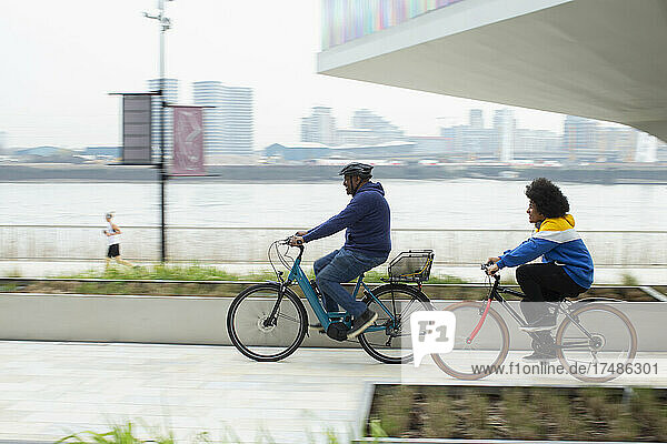 Father and son riding bicycles along urban waterfront  London  UK