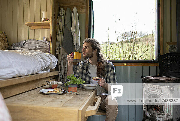 Junger Mann isst und trinkt in einer kleinen gemieteten Hütte