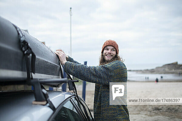 Lächelnder junger Mann  der am Strand ein Kanu am Auto befestigt