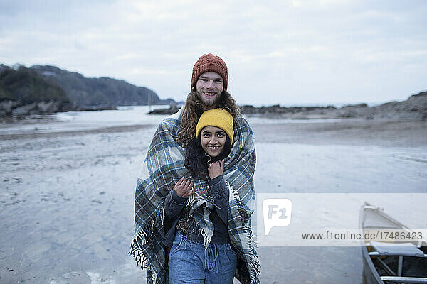 Portrait glückliches junges Paar eingewickelt in eine Decke am Strand