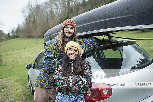Portrait happy young couple outside car with canoe on top