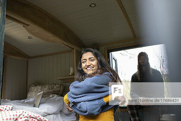 Glückliche junge Frau beim Ausziehen eines Pullovers in einer winzigen Miethütte
