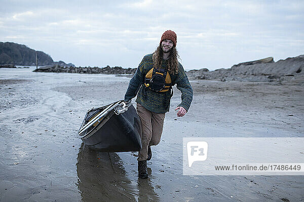 Portrait young man pulling canoe on wet sand beach