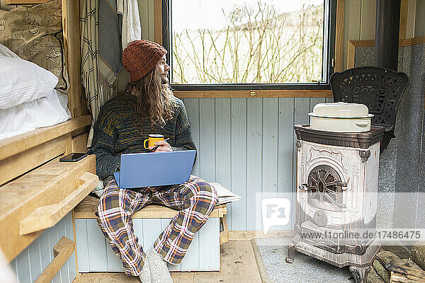 Nachdenklicher junger Mann benutzt Laptop in einer kleinen gemieteten Hütte