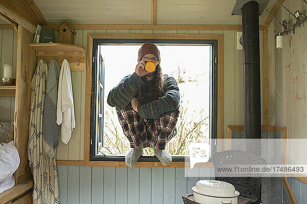 Junger Mann im Schlafanzug trinkt Kaffee in einem kleinen Kabinenfenster
