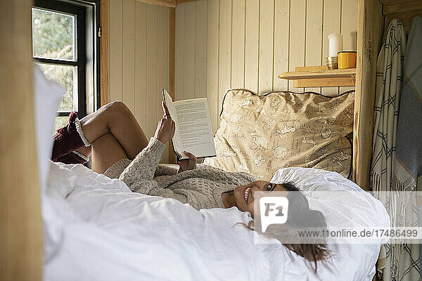 Portrait carefree young woman reading book in cabin rental bed