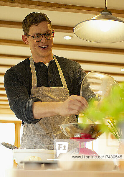 Smiling man baking using scale in kitchen