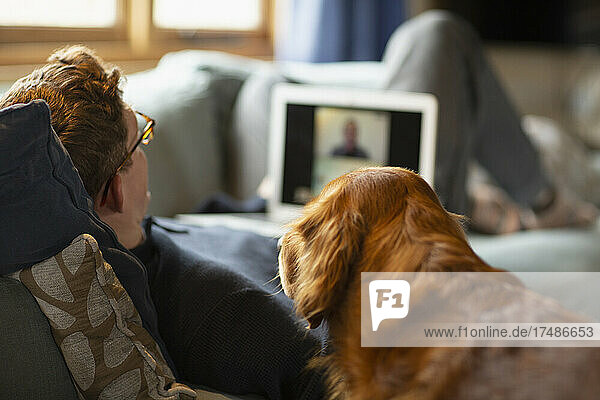 Man with dog video chatting with laptop on sofa