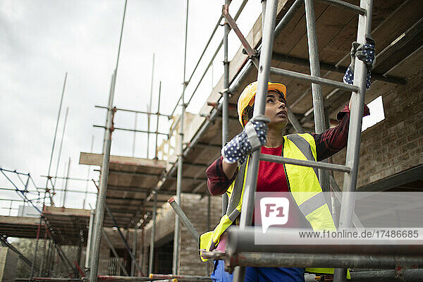 Weiblicher Bauarbeiter klettert auf einer Baustelle auf eine Leiter