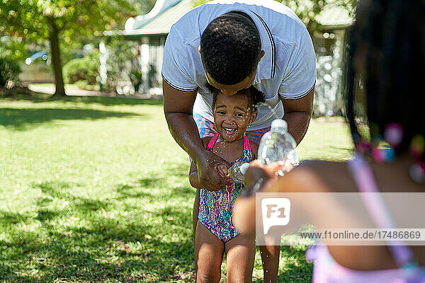 Vater und Töchter spielen mit Wasserspritzflaschen im Park