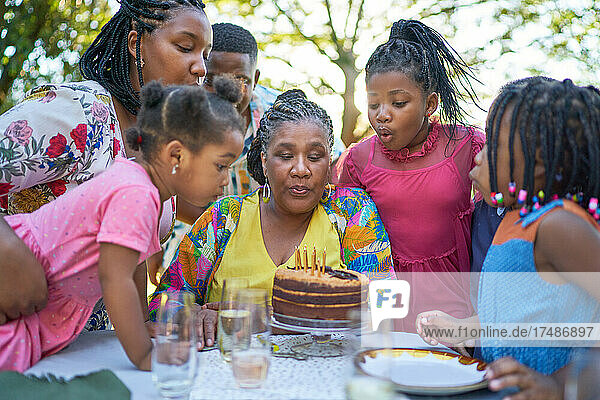 Mehrgenerationenfamilie bläst Geburtstagskerzen auf dem Terrassentisch aus