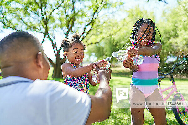 Verspielter Vater und Töchter mit Spritzwasserflaschen im Sommerpark