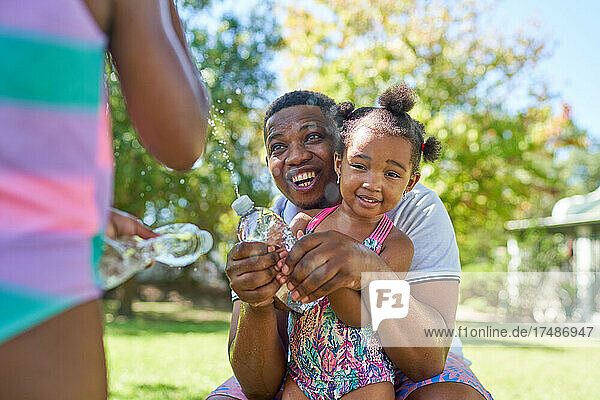 Fröhlicher Vater und Töchter spielen mit Spritzwasserflaschen